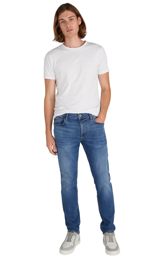 A man modeling a white crew-neck t-shirt and blue slim-fit jeans with white sneakers, standing against a solid white background.