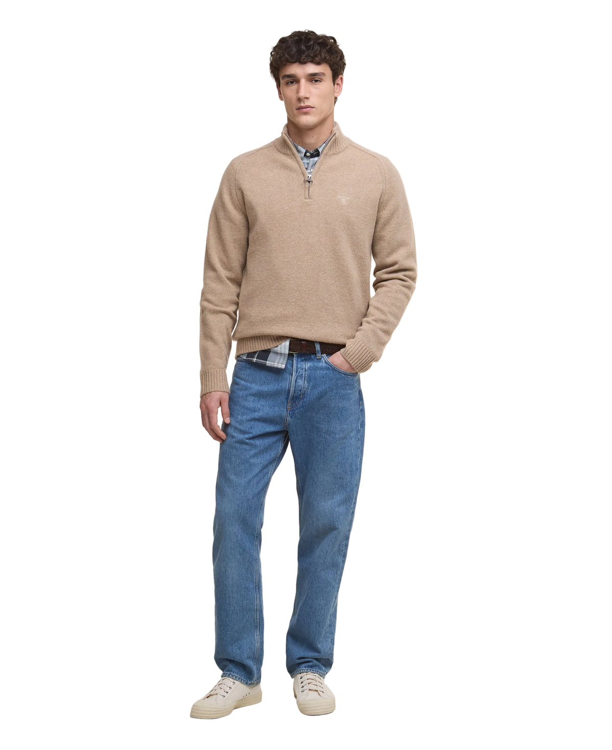 Man wearing a beige sweater, blue jeans, and white shoes on a white background