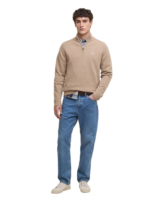 Man wearing a beige sweater, blue jeans, and white shoes on a white background